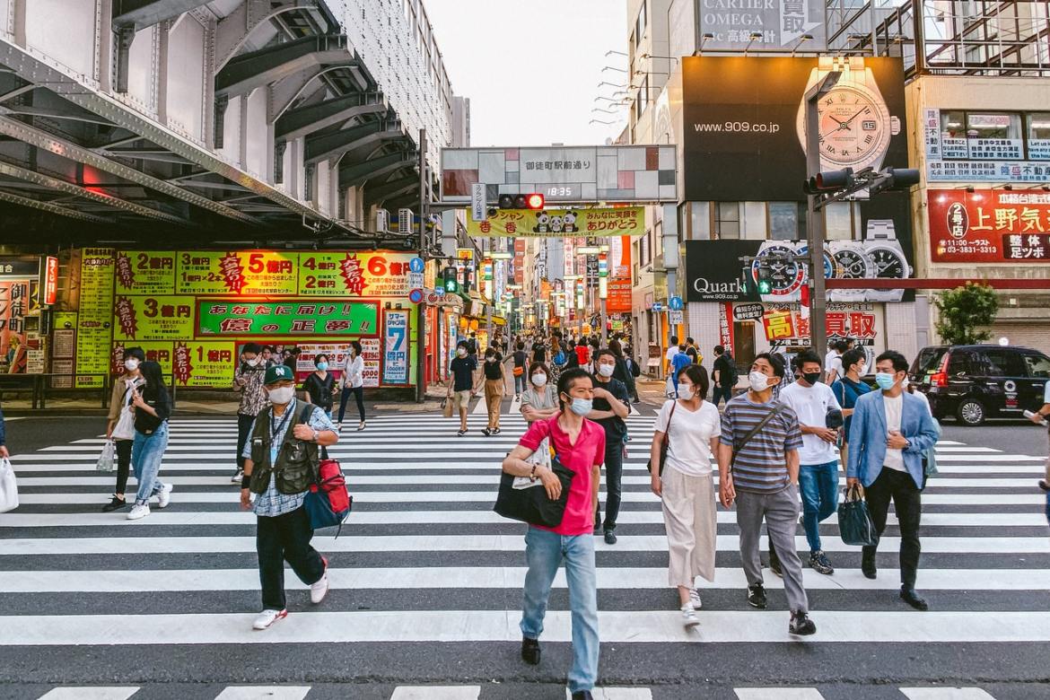 People cross a street in Taito-Ku, Tokyo with a shopping area in the background